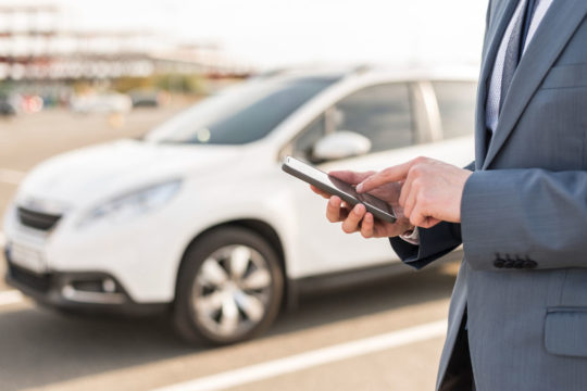 autónomo con móvil en la mano y coche de fondo