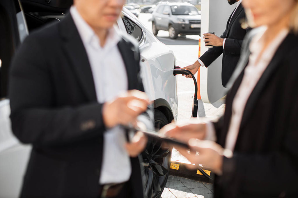 Personas de negocios hablando mientras recargan coche eléctrico de renting